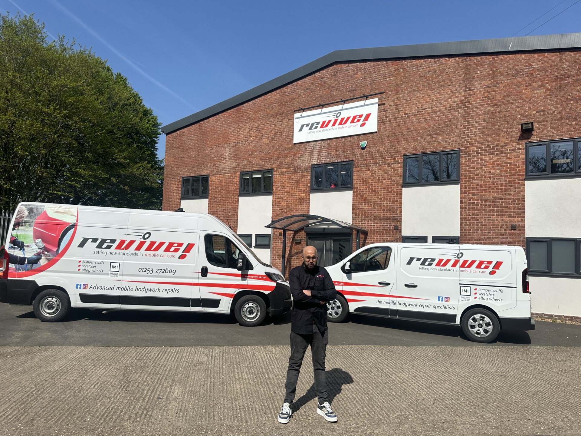 Mo standing outside head office building with two Revive! vans